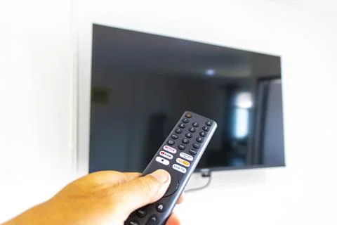 Hand holding a remote control while turning on a television Thailand. Stock Photos