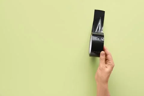 Hand holding a roll of black electrical tape with a strip unrolled on a light Stock Photos