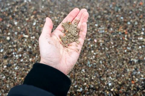 Hand holding sand mixed with microplastic against sandy sea shore in cold w.. 스톡 사진
