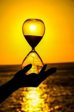 A hand holding a sand timer with the sun in the background Stock Photos