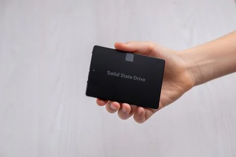 Hand holding SATA solid state drive against neutral background, modern comp.. Stock Photos