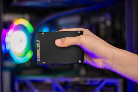 Hand holding SATA solid state drive in front of gaming computer with RGB li.. Stock Photos