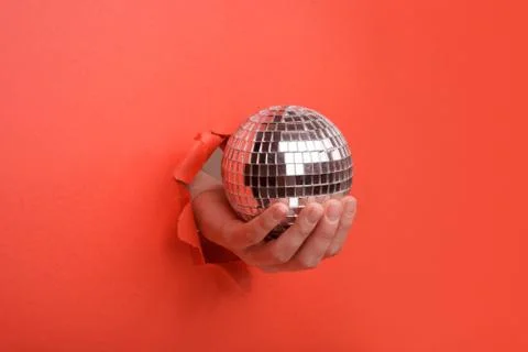 Hand holding Silver disco mirror ball on torn red paper wall. Copy space asid Stock Photos