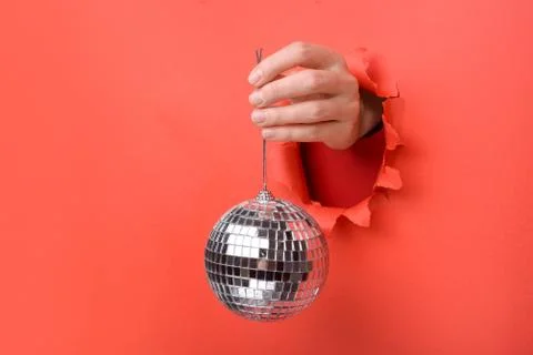 Hand holding Silver disco mirror ball on torn red paper wall. Copy space asid Stock Photos