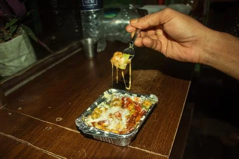 Hand holding silver fork with piece of cheesy savory food item Stock Photos