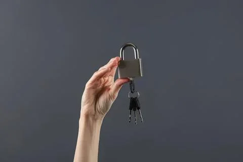 Hand holding silver lock with keys against gray background Stock Photos