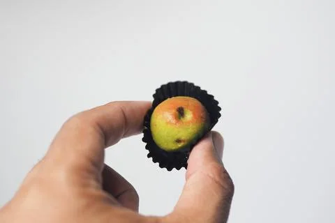 Hand holding a single apple-shaped cookie in a black paper liner against a .. Stock Photos