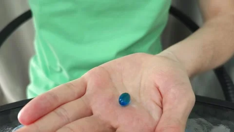 Hand holding a single blue pill. Close-up view of a person presenting medication Stock Footage 284042917