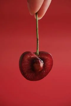 Hand holding single red cherry on red background Stock Photos
