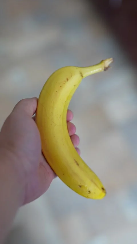 A hand holding a single ripe yellow banana, blurred background Stock Footage 332750488