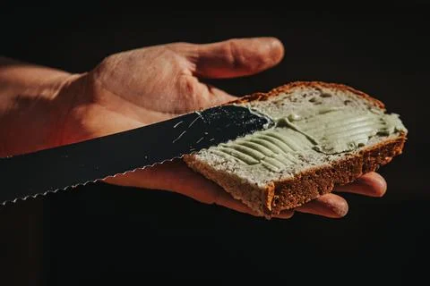 Hand holding slice of bread with green spread being applied using a serrate.. Stockfoto's