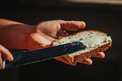 Hand holding slice of brown bread with spread, knife gliding across the sur.. Stockfoto's