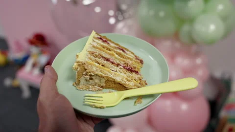 Hand holding slice of layered cake on pastel plate with plastic fork at festive Stock Footage 345608173