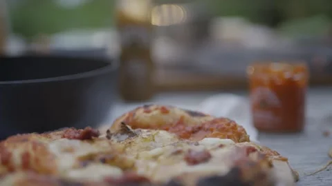 A hand is holding a slice of pizza with a jar of sauce next to it Stock Footage 297843545