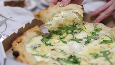 A hand holding a slice of pizza topped with olives, arugula, ham, and melted Stock Footage 302673281