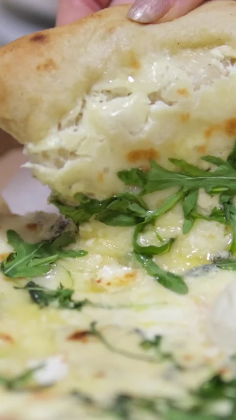 A hand holding a slice of pizza topped with olives, arugula, ham, and melted Stock Footage 303487043
