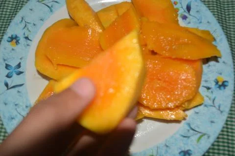A hand is holding a slice of yellow mango Stock Photos