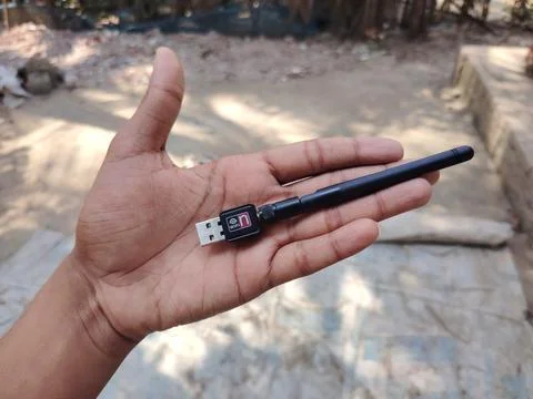 A hand holding a small black WiFi USB wireless adapter outdoors on a sunny .. Stock Photos