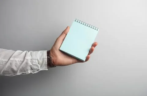 Hand holding a small blue notepad in front of plain gray background Foto stock