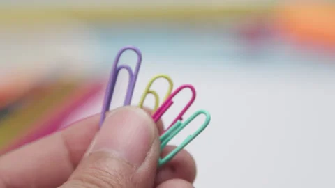 Hand holding a small bundle of pastel paper clips against a blurred background Stock Footage 337882731
