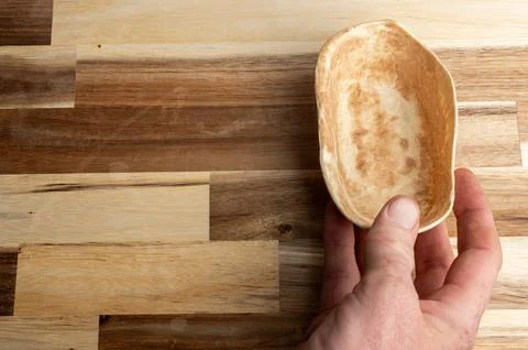 A hand holding a small, empty, natural wooden bowl on a wooden surface Stock Photos