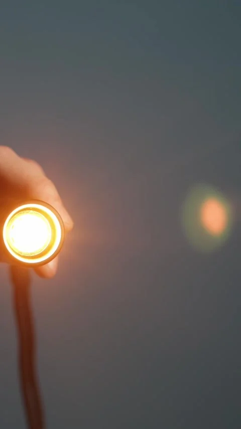 Hand holding a small flashlight with a warm orange glow, illuminating the Stock-Footage 343838078