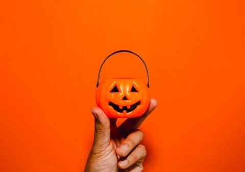 Hand holding small jack-o'-lantern pumpkin candy bucket, isolated on orange.. Фото