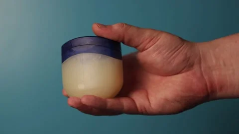 Hand holding a small jar of petroleum jelly against a blue background Stock Footage 340265476