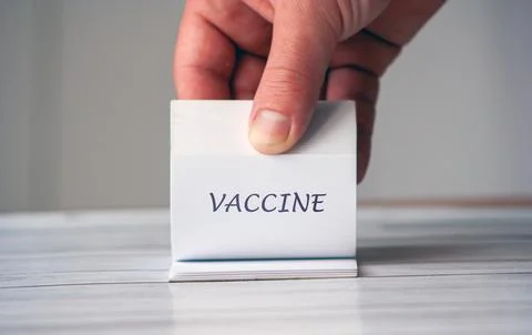A hand holding a small notepad displaying the word VACCINE. This image Foto stock