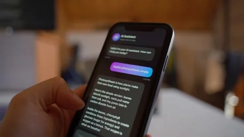 Hand holding smartphone asking AI assistant to explain photosynthesis for Vídeos de archivo 341406592