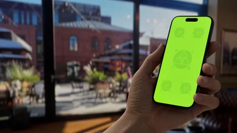 A hand holding a smartphone in a bright cafe setting during the day Stock Footage 296943347