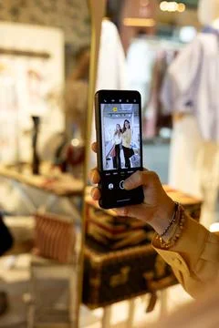 Hand holding smartphone capturing mirror selfie in boutique Stock Photos