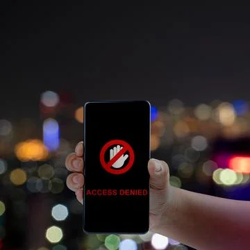Hand holding a smartphone displaying an Access Denied message and stop icon.. Stock Photos