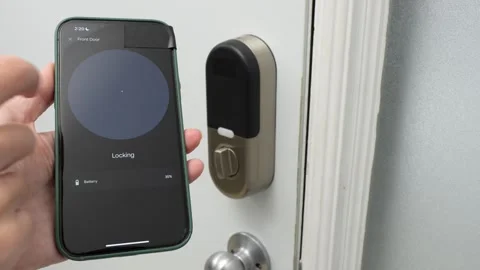 Hand holding smartphone displays locking interface for smart door lock Stock Footage 332578484
