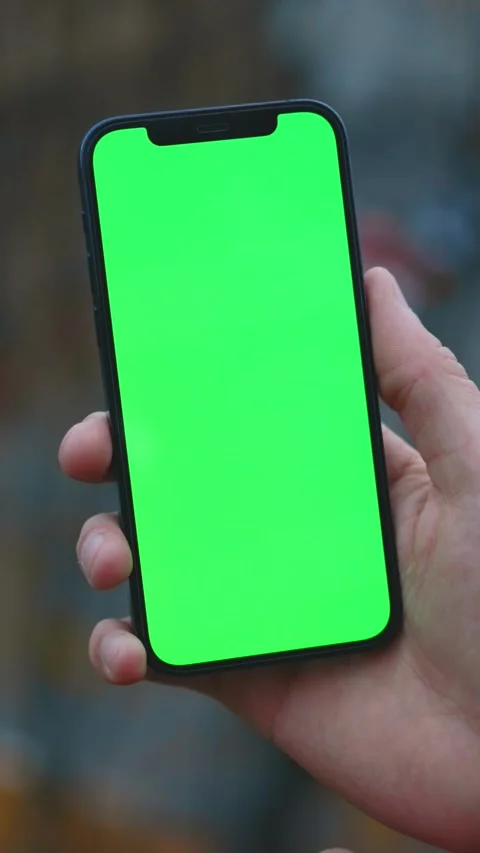 A hand is holding a smartphone that features a green screen, allowing for easy Stock Footage 314151360