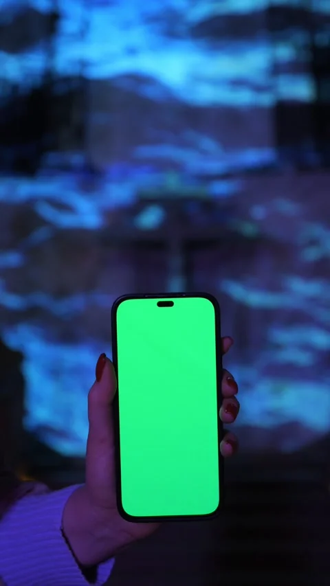A hand is holding a smartphone that features a vibrant green screen against an Stock Footage 281425930