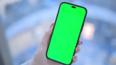 Hand holding smartphone with green screen in bright office, representing digital 스톡 동영상 277968322