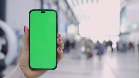 A hand holding a smartphone with a green screen in an airport terminal among Stock Footage 279907836
