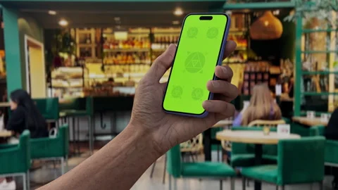 Hand holding smartphone with green screen in a cozy cafe Stock Footage 295209569