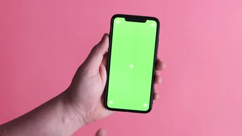 Hand holding a smartphone with a green screen and tracking markers on a pink Stock Footage 339189254