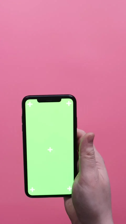 Hand holding a smartphone with a green screen and tracking markers on a pink Stock Footage 339189659
