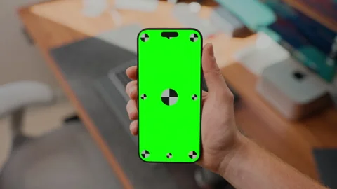 Hand Holding Smartphone with Green Screen Mockup in Modern Office Workspace Stock Footage 345846863