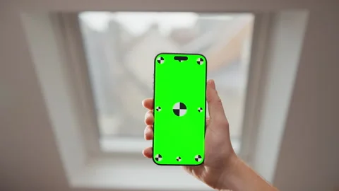 Hand Holding Smartphone with Green Screen Mockup by Indoor Window in Bright Room Stock Footage 345847132