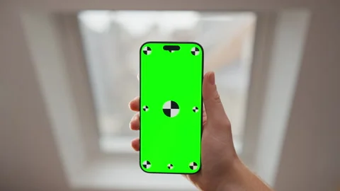 Hand Holding Smartphone with Green Screen Mockup by Window in Indoor Daylight Stock Footage 345849896