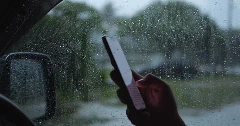 Hand Holding Smartphone Inside Car Beside Rain-Covered... Stock Footage 332075271