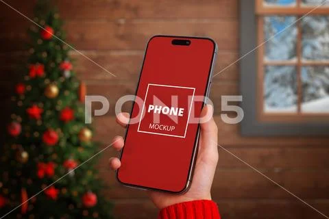 Hand holding smartphone mockup in front of Christmas tree PSD Template