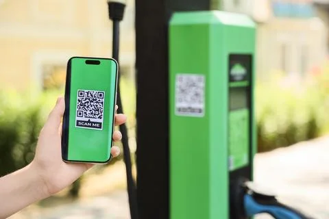 Hand holding smartphone with QR code near electric vehicle charging station Foto stock
