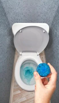 Hand holding solid detergent is put in toilet bowl tank. 스톡 사진