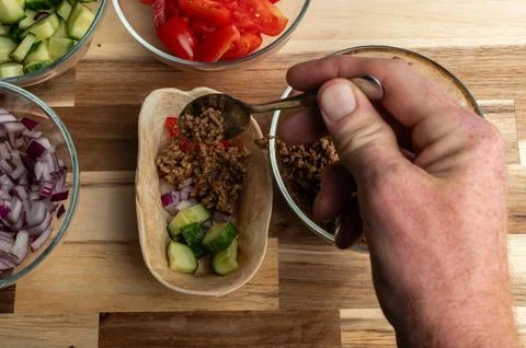 A hand holding a spoon adding ground meat to a small bowl, surrounded by fr.. Stock Photos