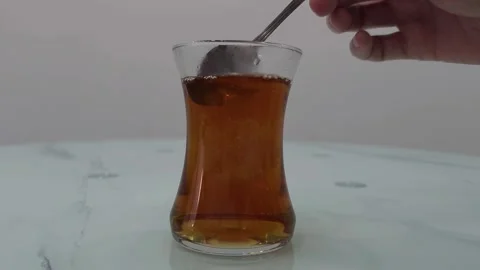 Hand holding a spoon of sugar over a glass of tea. Beverage preparation concept. Stock Footage 282610956